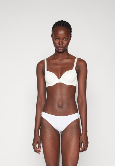 Soutien-gorge rembourré blanc avec bretelles réglables, bonnets moulés et texture lisse. Assorti à un slip bikini blanc avec un petit nœud décoratif.