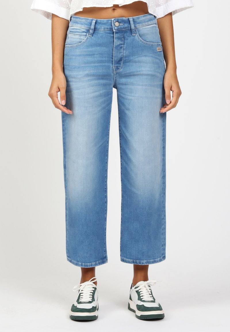 Helle blaue Denim-Hose mit weitem Bein und hoher Taille, ausgestattet mit fünf Taschen und subtilen Verwaschungen, kombiniert mit grünen und weißen Sneakern.
