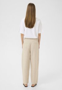 Beige linnen broek met een ontspannen pasvorm, met een hoge taille en twee achterzakken, gecombineerd met een witte top met korte mouwen. Platte sandalen.