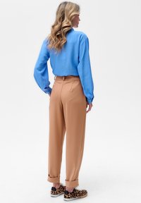 Niebieska, strukturalna koszula z długim rękawem w komplecie z dopasowanymi, beżowymi spodniami z podwijanym dołem, noszona z pantoflami w leopardzi wzór.