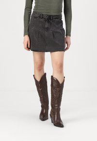 Stivali da cowboy in pelle marrone con tacchi alti e design embossato, abbinati a una minigonna in denim grigio aderente.