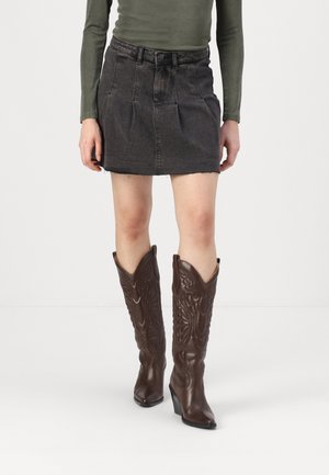 Stivali da cowboy in pelle marrone con tacchi alti e design embossato, abbinati a una minigonna in denim grigio aderente.