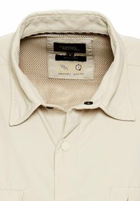 Beige leichtes Hemd mit einem atmungsaktiven Mesh-Kragen, schnelltrocknendem Stoff, zwei schwarzen Knöpfen und einem regulären Passform-Etikett im Inneren.