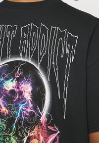 Černé bavlněné tričko s živým, mnohobarevným grafickým designem s kosmickým motivem, tučným bílým textem a volným střihem.