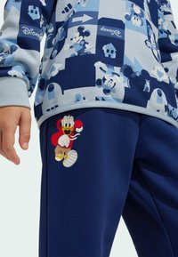 Niebieska bluza z długim rękawem z nadrukiem Myszki Mickey; granatowe spodnie z grafiką Kaczora Donalda z czerwonym akcentem na udzie. Miękka struktura materiału.
