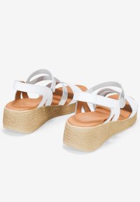 Sandalia blanca con múltiples correas, tacón de cuña envuelto en yute natural. Parte superior de cuero suave y plantilla acolchada de color marrón.