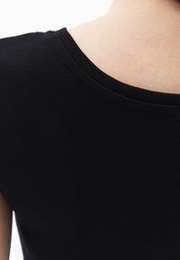 Svart ribbad tyg, med en vid halsringning och slät textur, som visar baksidan av en åtsittande topp med en subtil lyster.