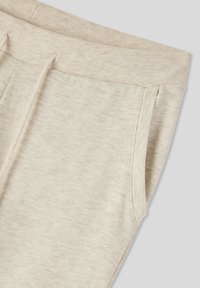 Pantaloni della tuta beige chiaro con vita a costine, tasche laterali e tessuto morbido e texture. Design semplice senza motivi o dettagli.