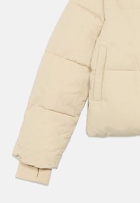 Beige polstret jakkeærme med vandret syninger og en ribbet manchet med en tommelhul, lommeåbning synlig på jakkehegnet.