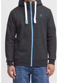 Grijze zip-up hoodie met een blauwe ritssluiting en witte trektouwen. Heeft een voorzak en een blauw logo op de borst. Ribgebreide manchetten en onderrand.