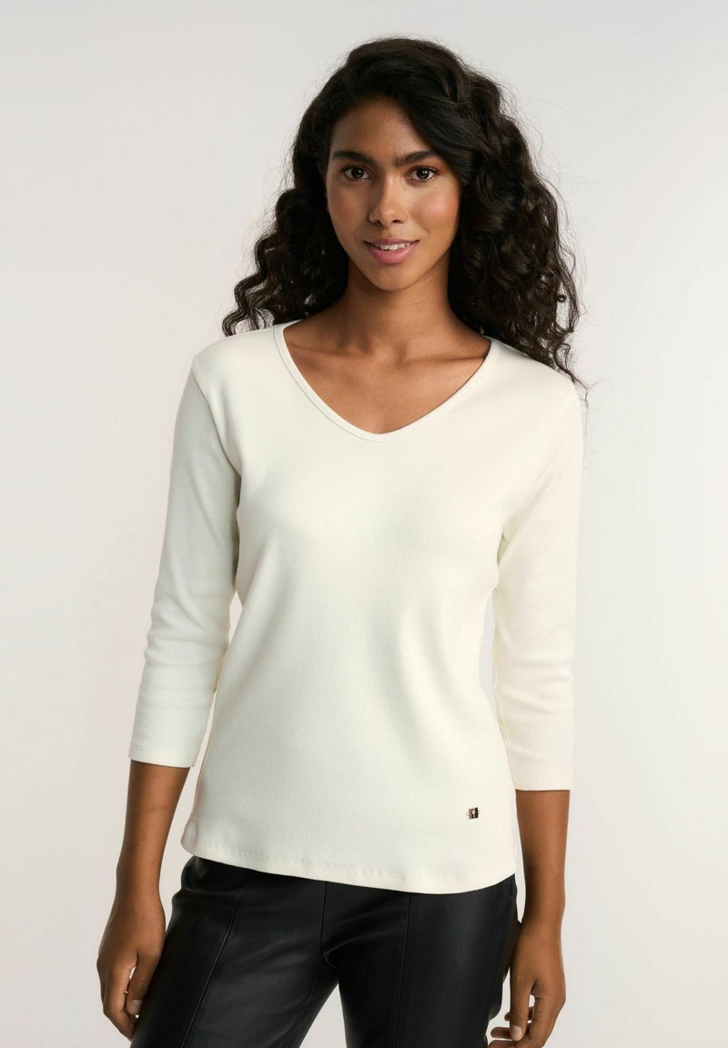 Biała, żebrowana, dzianinowa bluzka z długim rękawem i dekoltem w kształcie litery V, z małym logo akcentującym na dolnym brzegu i gładką teksturą.