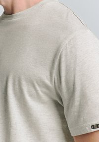 Lichtgrijs T-shirt met korte mouwen, gemaakt van zacht, gestructureerd stof; heeft een ronde halslijn en een zwart label bij de mouw.