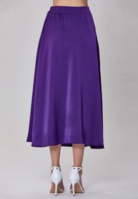 Jupe A-line en satin violet avec une texture lisse et une taille élastique, tombant à mi-mollet. Associe à des sandales à talons blancs.