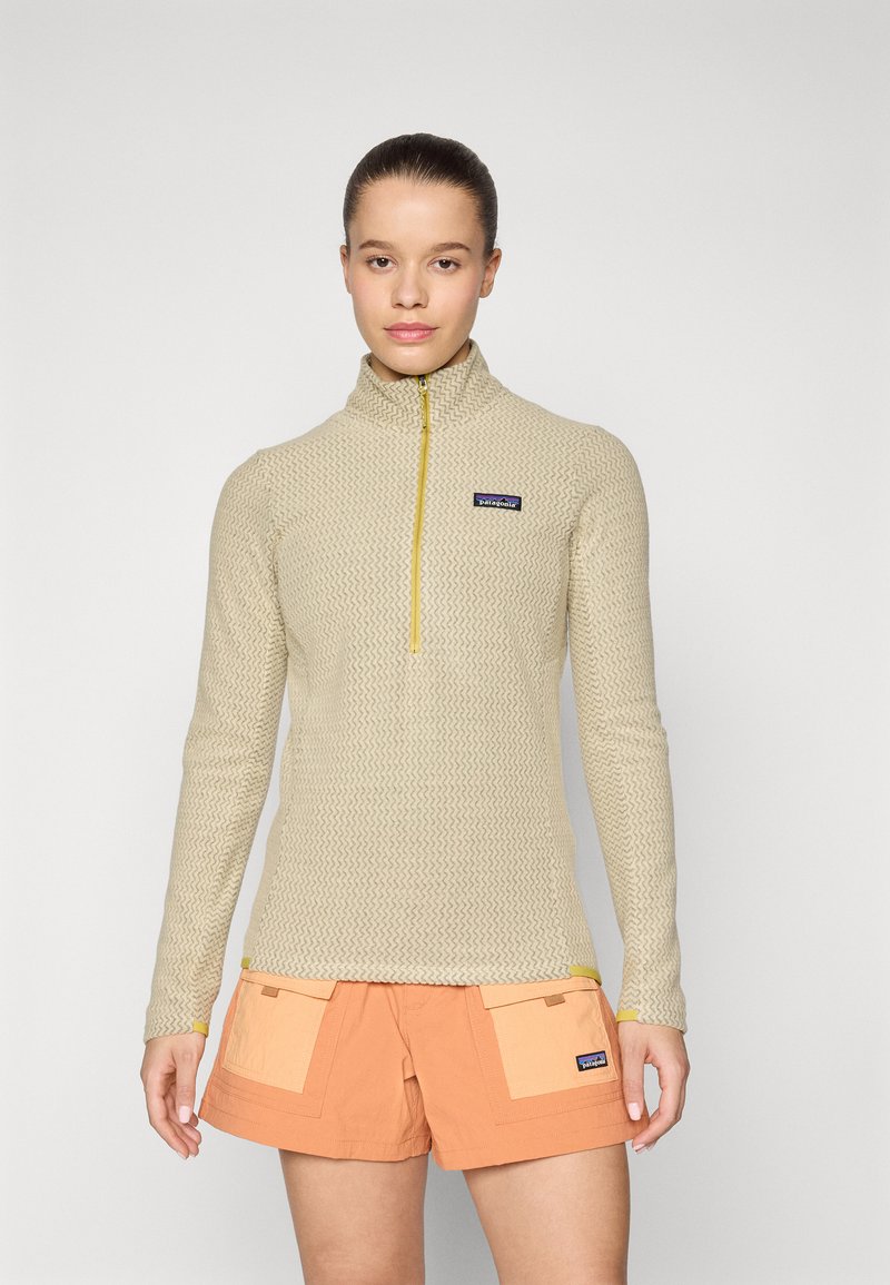 Pullover beige con zip a un quarto e motivo intrecciato, dotato di zip gialla. Un paio di pantaloni corti arancioni con tasche a contrasto, entrambi con logo del brand.