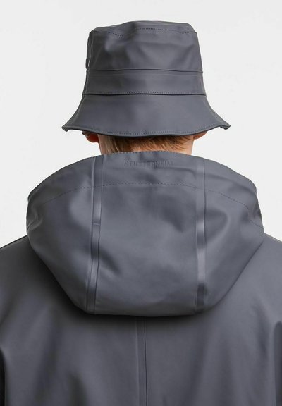 Grau wasserfester Bucket-Hut kombiniert mit einem grauen wasserfesten Mantel, der einen hohen Kragen und eine glatte Textur aufweist, mit dezentem Branding auf der Rückseite.