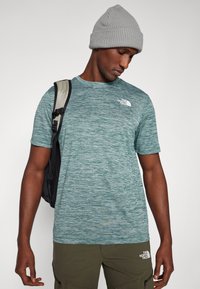 Lühikeste varrukatega, teeelrohelise hekseldatud t-särk ümmarguse kaelusega, millel on vasakul rinnal väike valge logo ja see on paaritatud oliivroheliste cargo-lühikarvatustega pükstega.