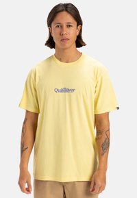 Camiseta de algodón amarilla con mangas cortas, que presenta un logo azul en el pecho. Textura suave, corte relajado y sin patrones distintivos.