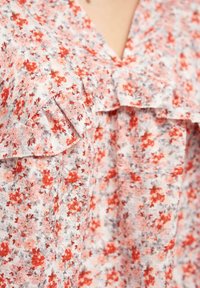 Blusa floreale realizzata in un tessuto leggero con fiori rossi e grigi, collo a V e un bordo arricciato lungo il colletto e le spalle.