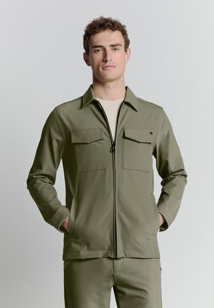 Olijfgroene ritsjack met twee borstzakken, lange mouwen en een kraag. Gladde stof met een gestructureerd ontwerp, gecombineerd met bijpassende broek.
