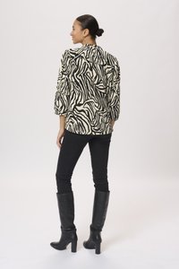 Zebra-print blouse in crème en zwart, met een relaxte fit en pofmouwen, gecombineerd met strakke zwarte jeans en knie-hoge zwarte laarzen.