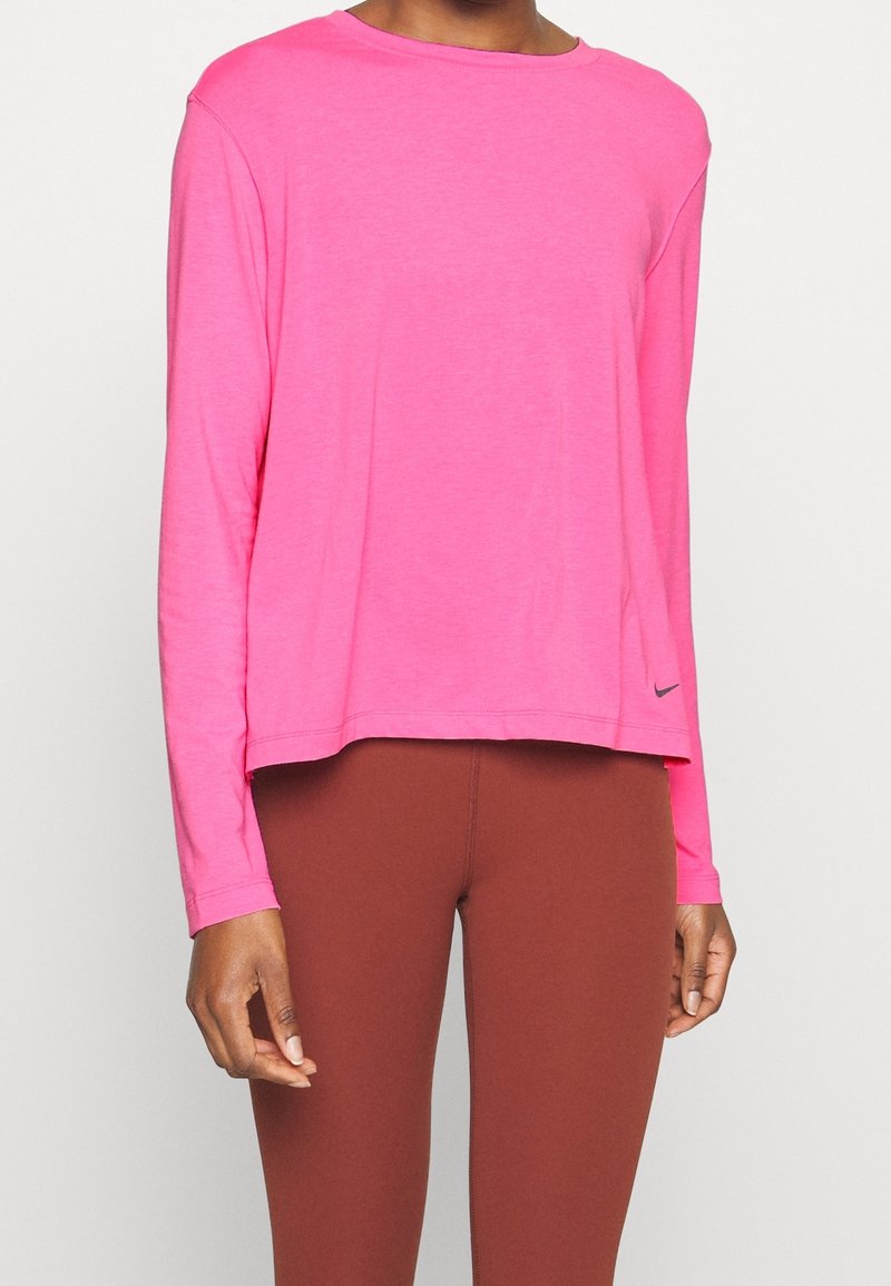 Långärmad rosa skjorta i lätt material, med rundad halsringning, lös passform och liten svart Nike-logotyp på nedre högra sidan.