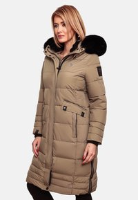 Manteau rembourré beige avec une capuche à fourrure noire, poches zippées et un design matelassé horizontal. Présente un patch logo sur le bras.