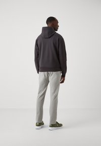 Felpa con cappuccio grigio scuro, pantaloni tuta grigi e sneakers verdi. Tessuto morbido con una vestibilità rilassata e polsini e vita a costine sulla felpa.
