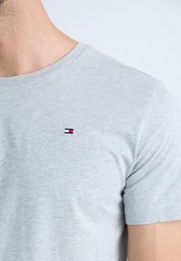 T-shirt in cotone grigio con collo a giro, dotata di un piccolo logo ricamato in blu navy, rosso e bianco sul lato sinistro del petto. Maniche corte.