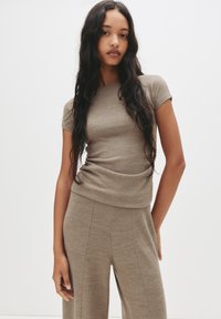 Kortærmet taupe strikbluse med en let afslappet pasform, der har en glat overflade og en subtil draperingsdetalje ved taljen.