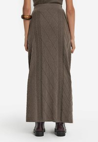 Brun stickad maxikjol med diamantmönster och texturerade detaljer. Har hög midja och en golvlång design, kombinerad med ankelboots.