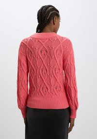Maglione rosa a maglia con un motivo a rombi testurizzati, maniche lunghe e orlo a coste. Presenta dettagli a maglia aperta lungo la schiena.