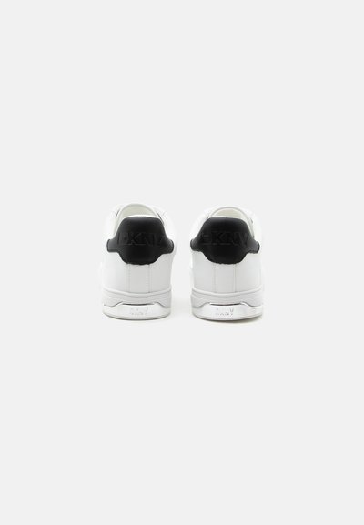 Baskets blanches avec des languettes de talon noires, logo DKNY embossé sur les languettes de talon et détail du logo argenté sur la semelle intermédiaire, vues de dos.