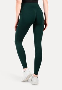 Donkergroene leggings met een hoge taille, een gladde textuur en een volledig ontwerp, gecombineerd met witte sportschoenen.