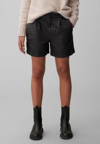 Černé kožené šortky s volným střihem, s bočními kapsami a podhrnutým lemem. Kombinované s černými kotníkovými botami a béžovým svetrem.