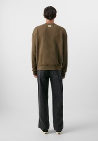 Oliven grønn sweatshirt med avslappet passform, ribbestrikkede mansjetter og hem; kombinert med løstsittende svarte jeans og beige sneakers.