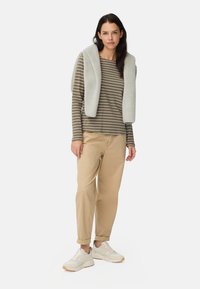 Chemise à manches longues rayée en vert et beige, associée à un pantalon beige et un gilet en polaire gris. Baskets blanches avec une semelle en caoutchouc.