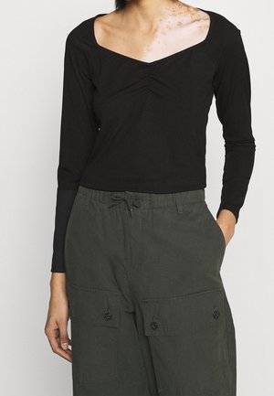 Haut noir à manches longues avec un décolleté carré, présentant un léger fronce au centre. Associé à un pantalon cargo vert olive avec des poches.
