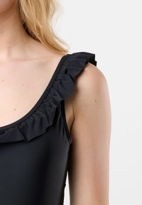 Zwarte zwempak met een gerimpelde schouderband langs de halslijn. Glad textuur met een afbeelding van een aansluitend ontwerp, met een klassieke tankvorm.