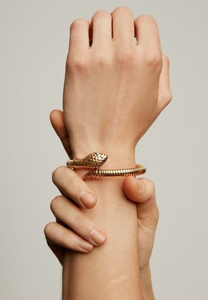 Pulsera en forma de serpiente de oro con una cabeza texturizada y una banda lisa enroscada. Usada en una muñeca, mostrando finos detalles y artesanía.