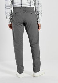 Pantalones grises con una textura suave, diseño de pierna recta y dos bolsillos traseros. Combinándolos con zapatillas blancas y una camisa estampada.