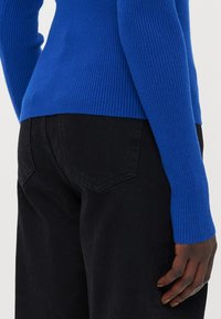 Tettsittende blå ribbestrikket genser med lange ermer, kombinert med høyt liv svarte denimjeans med klassisk lommendesign.