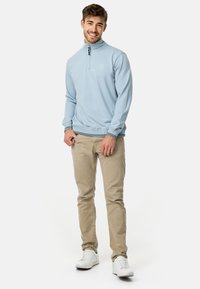 Lyseblå lynlåsstroptrøje med høj krave, ribbede manchetter og kant. Kombineret med beige bukser og hvide sneakers.