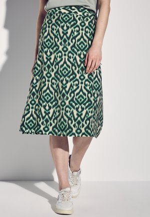 Ausgestellter Rock im grün-krämigen Ikat-Muster. Mittellang, elastischer Bund, weicher Stoff, kombiniert mit weißen Sneakers.