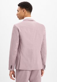 Lichtroze op maat gemaakte colbert met een enkele split, gekartelde revers en donkere knopen op de manchetten. Glad stof met een subtiele textuur.