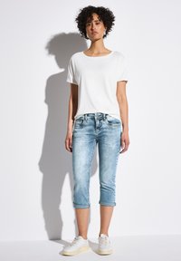 T-shirt blanc à manches courtes associé à un jean court bleu clair. Le jean présente des ourlets retroussés et un design à cinq poches. Des baskets blanches complètent la tenue.