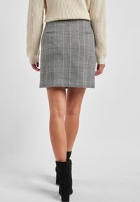 Falda de cuadros gris con un ajuste entallado, con cintura alta y patrones combinados de cuadros en negro y blanco. El modelo lleva botas de tobillo negras.