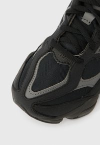 Black athletic shoe with mesh and textured fabric upper, featuring gray accents and a thick rubber sole, designed for comfort and breathability.