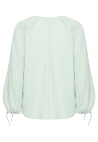 Blusa verde menta, con texture e vestibilità rilassata, maniche lunghe a palloncino e lacci ai polsini. Presenta un collo rotondo e plissé sul retro.