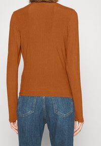 Brown ribbed long-sleeve top with a fitted silhouette and rounded neckline, paired with light blue denim jeans featuring a five-pocket design.