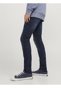 Vaqueros azul oscuro con un corte ajustado, con un ligero desgaste, diseño de cinco bolsillos y detalles de costura. Combinados con zapatillas de deporte marinas.